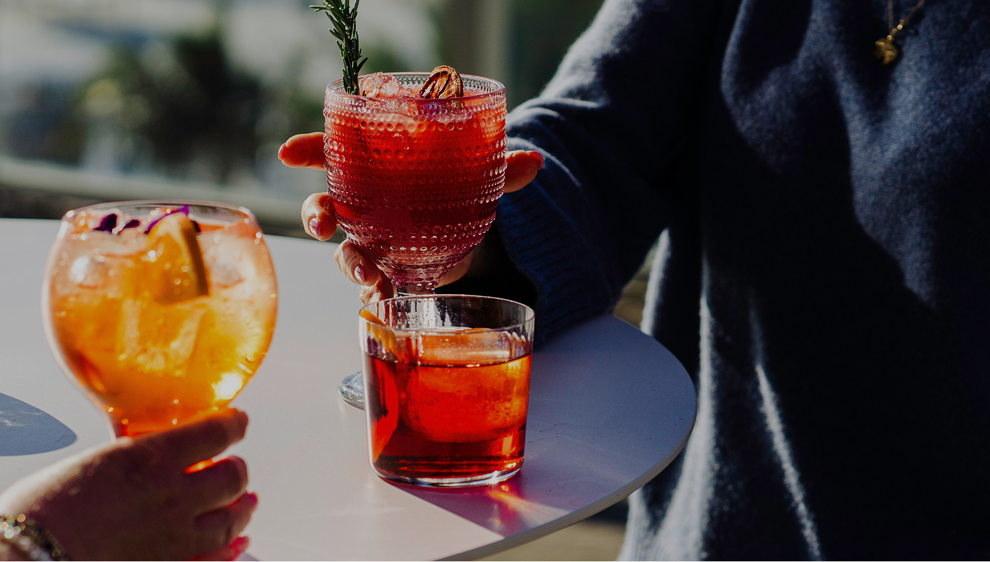 Two people holding cocktails on a table outdoors